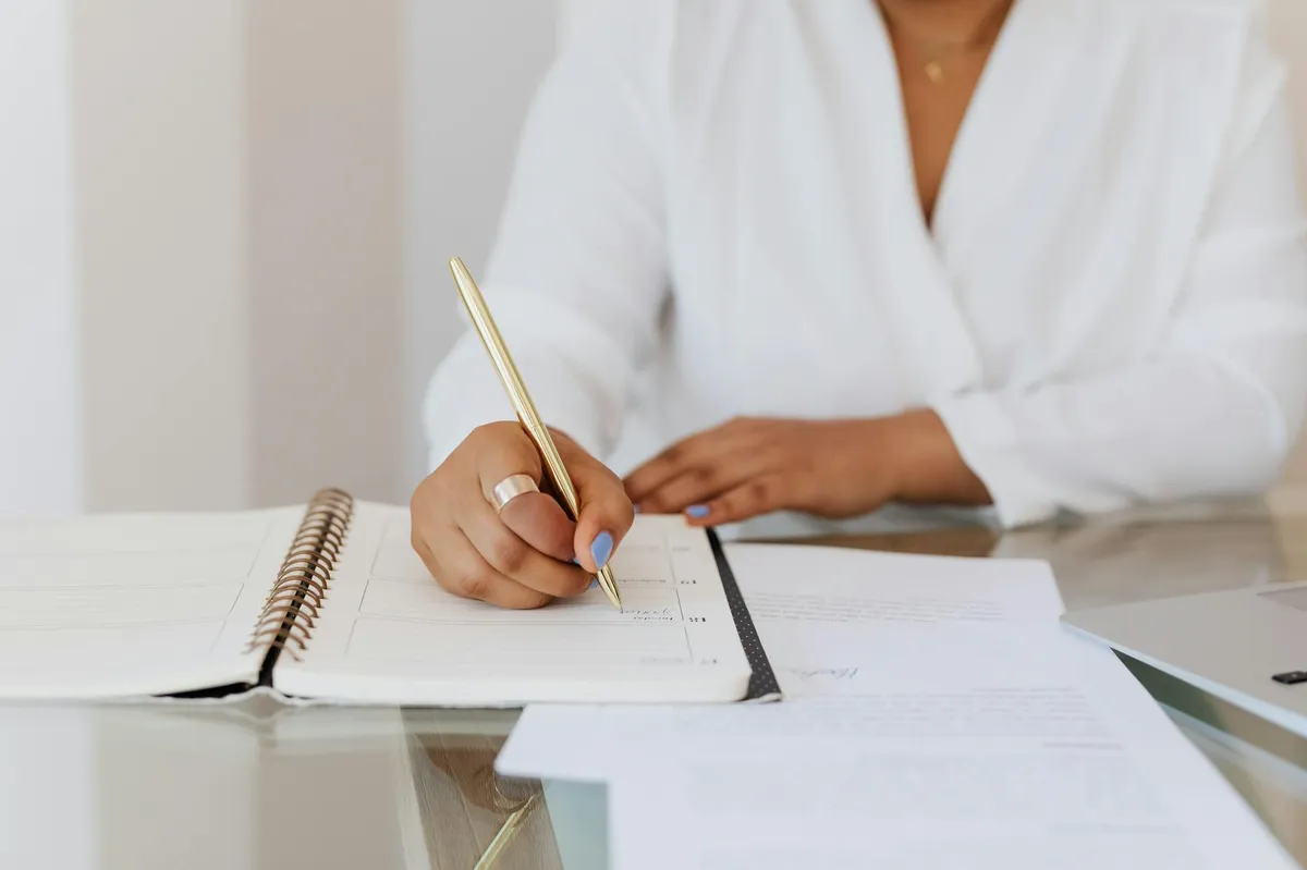 Empresário escrevendo anotações em caderno com computador aberto na mesa