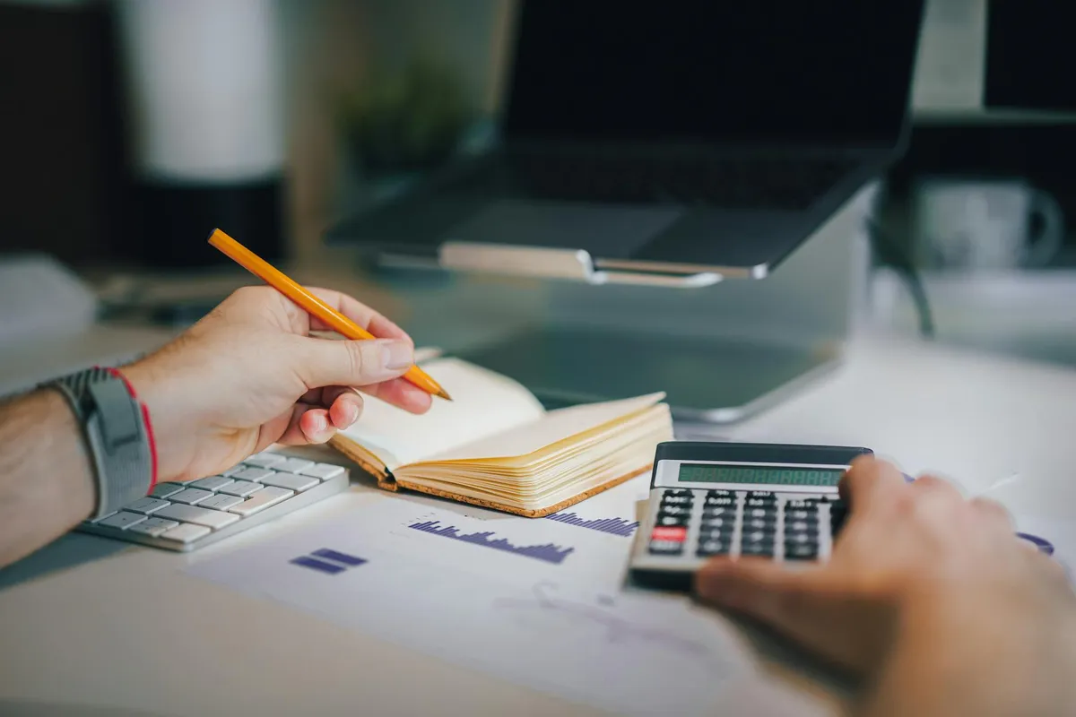 Pessoa verificando orçamento no computador com calculadora ao lado em mesa de trabalho