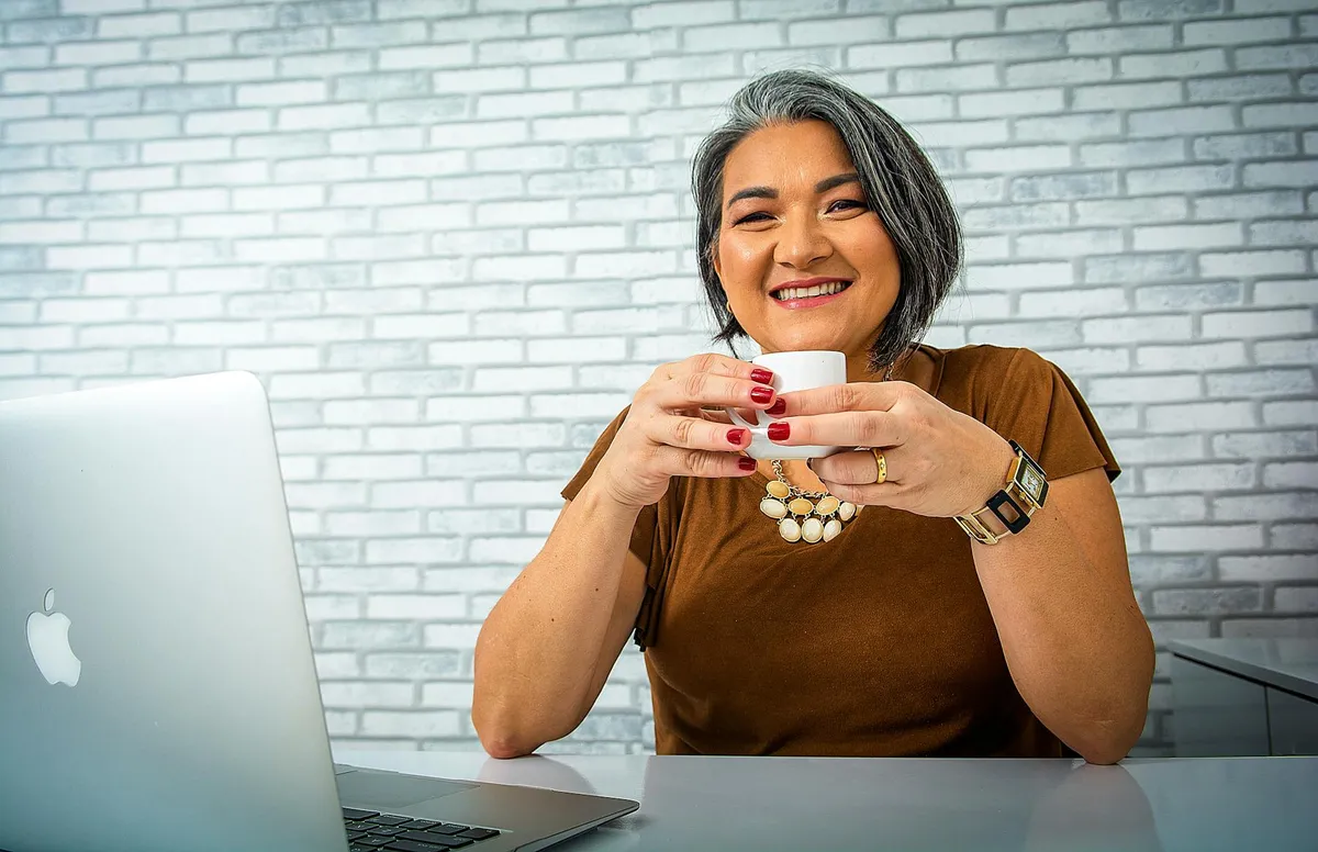 Pessoa de meia-idade sorrindo enquanto trabalha no laptop em ambiente de escritório simples