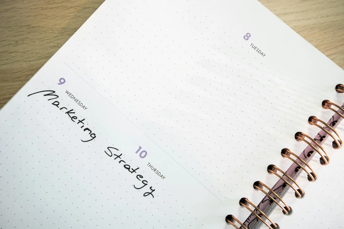Pessoa olhando para agenda e notebook com planner semanal visível na mesa
